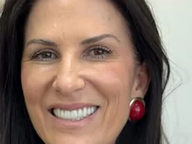 Leila Araes sorrindo no consultório, com estante ao fundo
